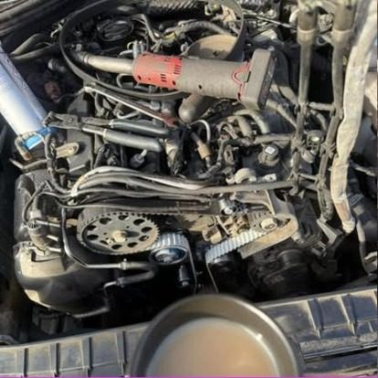A diesel engine bay with the timing cover off and the belt, tensioner and pulleys exposed, an air tool resting across the top of the engine.